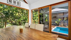 Una mesa de madera para comedor con seis sillas, puertas correderas de vidrio y vista a una piscina.