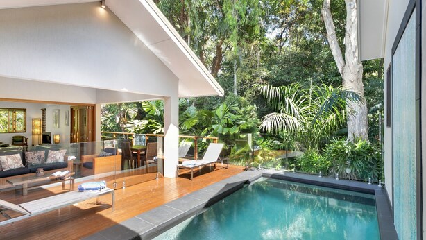 Un área de piscina interior moderna con balaustrada de vidrio, deck de madera y sillas de descanso.