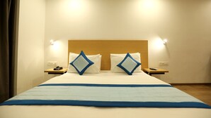 A hotel room with a large bed, two bedside tables, a wooden headboard, and wall-mounted lights. - Hotel Olive Saffron (New Delhi)