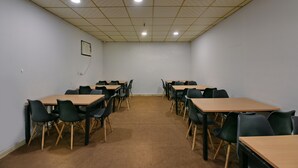 A conference room with multiple tables and chairs, a carpeted floor, and a grid-patterned ceiling with recessed lighting. - Hotel Olive Saffron (New Delhi)