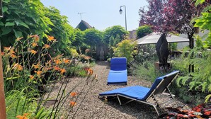 A garden with a blue lounge chair and a small table, surrounded by various plants and flowers. - Cozy cottage with garden and Wifi in Drevant (Drevant)