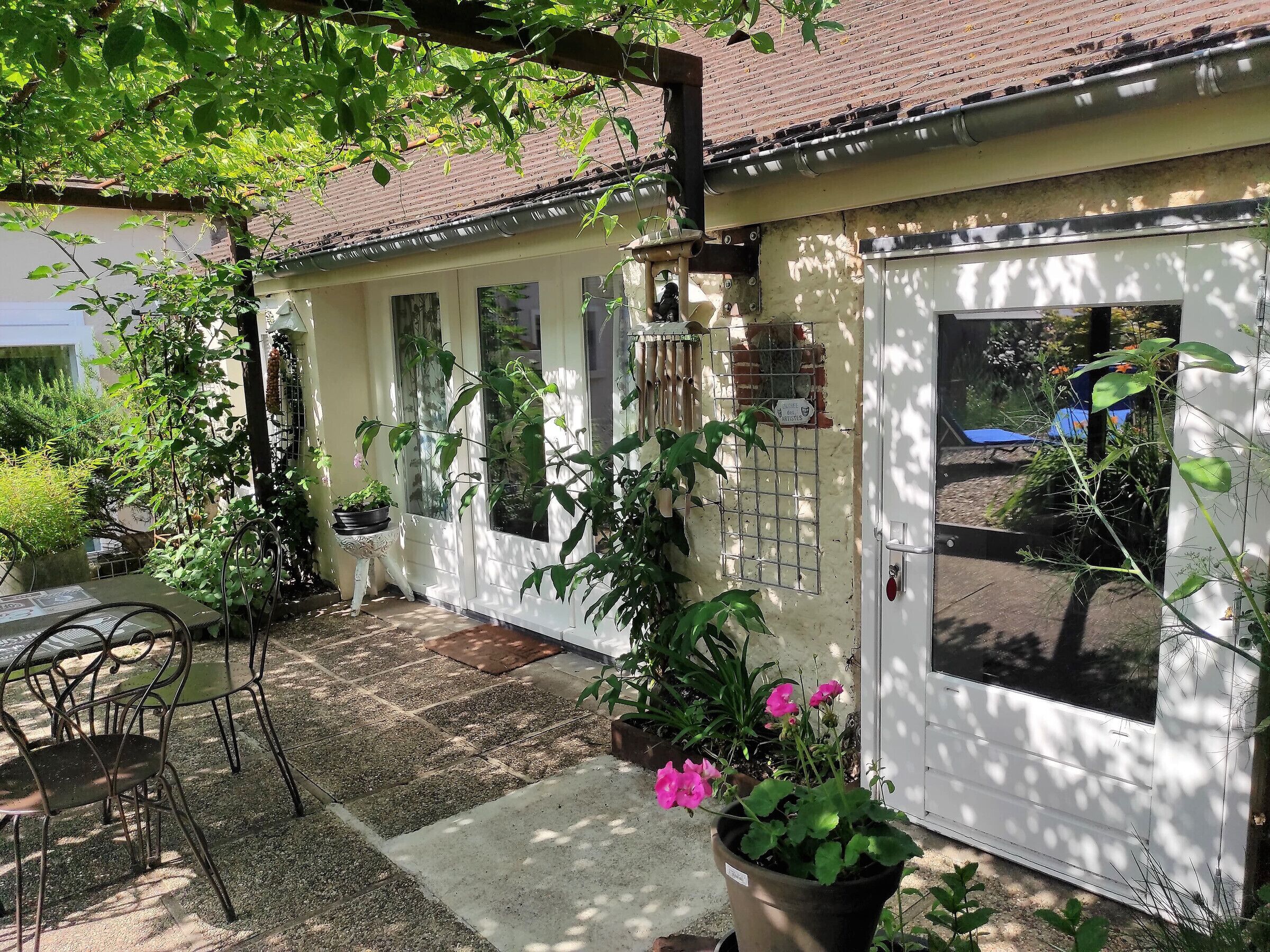 A covered patio area with a table and chairs, potted plants, and a white door with a window.