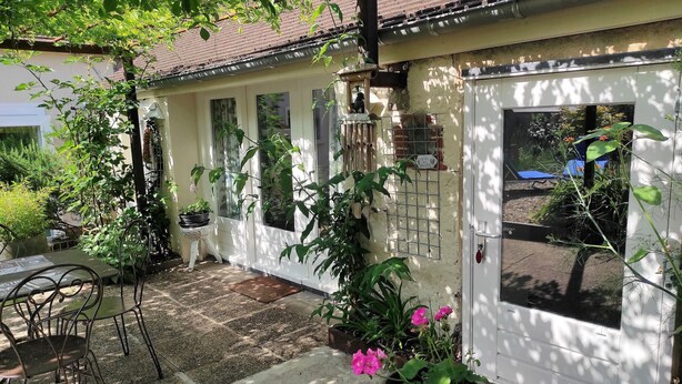 A covered patio area with a table and chairs, potted plants, and a white door with a window. - Cozy cottage with garden and Wifi in Drevant (Drevant)