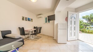 A compact living space with a dining area, a sofa, a glass-top table, and a refrigerator. - 100 metres to the crystal clear Adriatic Sea (Baska)
