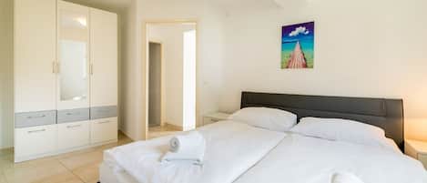 A hotel room with a bed, a wardrobe, a painting, and a door leading to another room.