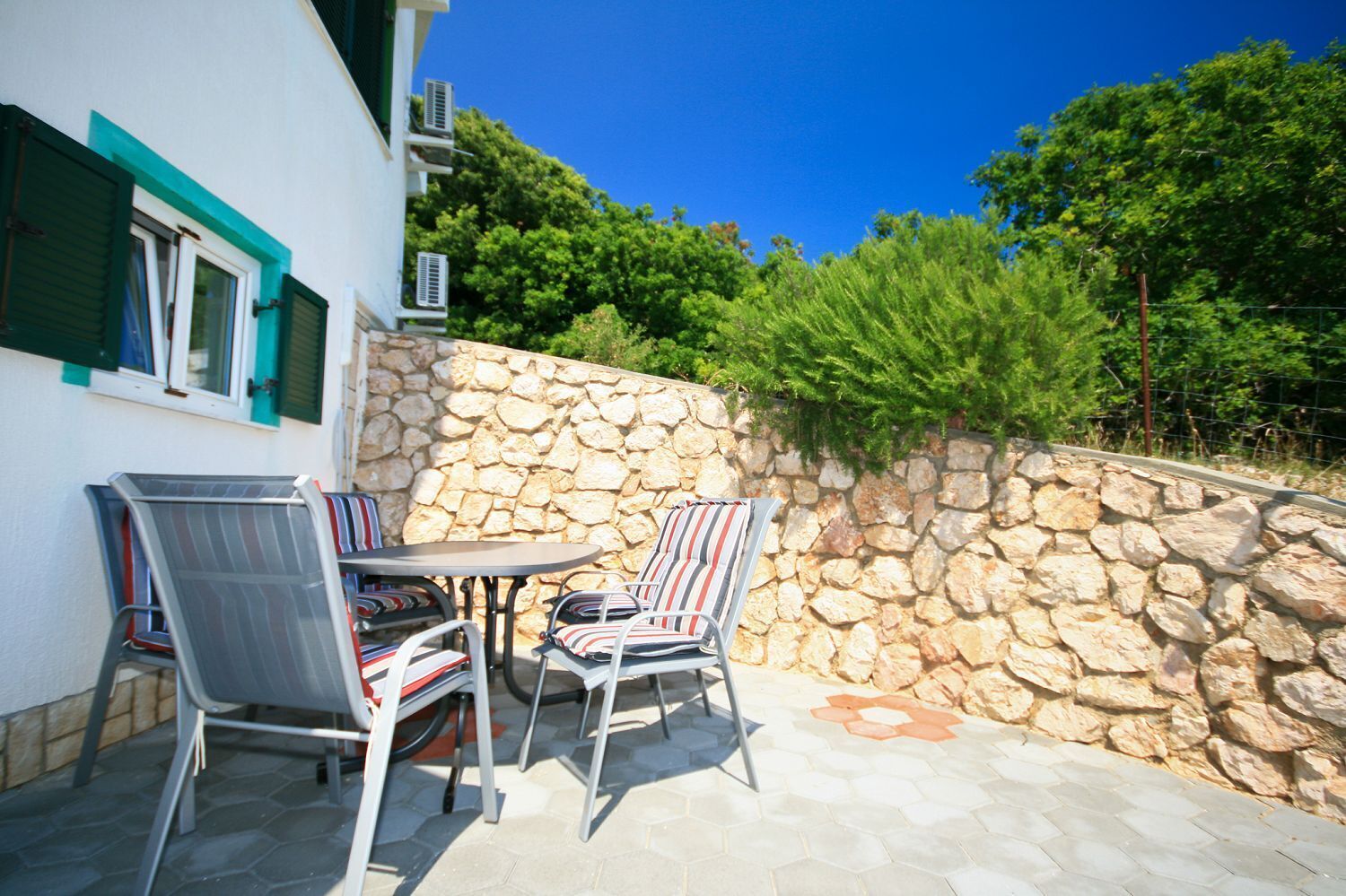 Une terrasse extérieure avec un mur en pierre, deux chaises et une table.