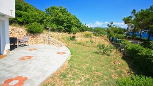 A patio with hexagonal tiles and orange flower patterns, a stone wall, a chair, and a table. - 100 metres to the crystal clear Adriatic Sea (Baska)