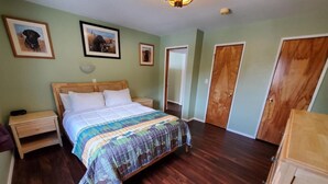 A bedroom with a wooden bed, a nightstand, a dresser, and a door. - {Forget-Me-Not Inn} Alaskan Waterfront Vacation Rental (Eagle Suite) (Sitka)
