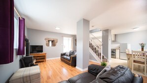 Een moderne woonkamer met een open haard, een bank, een televisie en een keuken die zichtbaar is door een open deur.