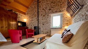A cozy living room with a stone wall, a wooden ceiling, a red chair, a white sofa, and a small table.