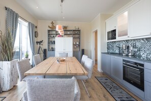 Una cocina moderna con armarios grises, una mesa de comedor de madera, sillas de mimbre y un salpicadero de azulejos.