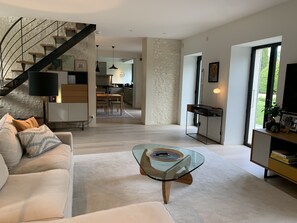 Uma sala de estar moderna com uma mesa de centro de vidro, um sofá e uma escada que leva a uma cozinha.