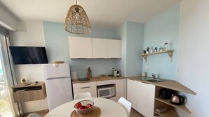 A compact kitchen with white cabinets, a white dining table with a woven placemat, and a hanging light fixture.