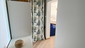 A hallway with a white partition, a woven basket, and a door leading to a room with a bed and blue furniture.