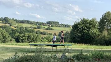 A trampoline in an outdoor setting with a grassy field and trees in the background.