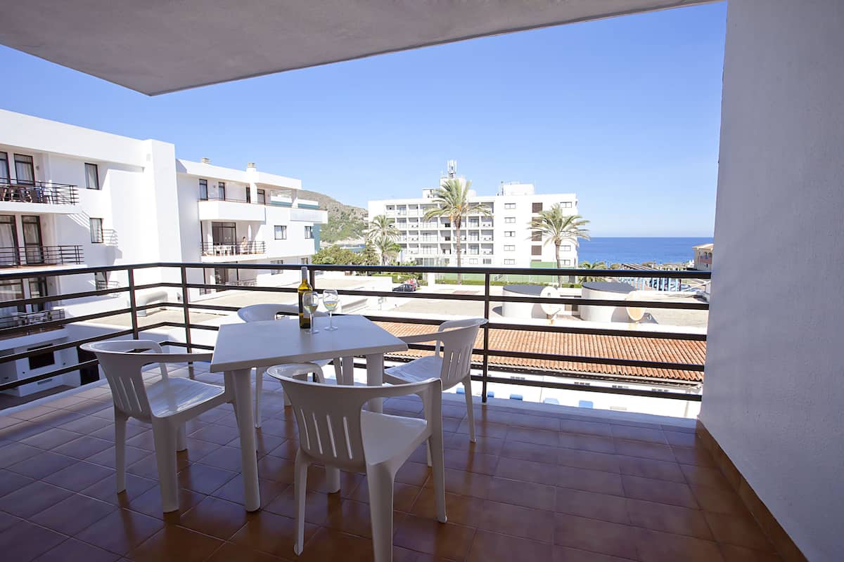 Un balcón con mesa y sillas, con vistas a una zona costera con edificios y palmeras.
