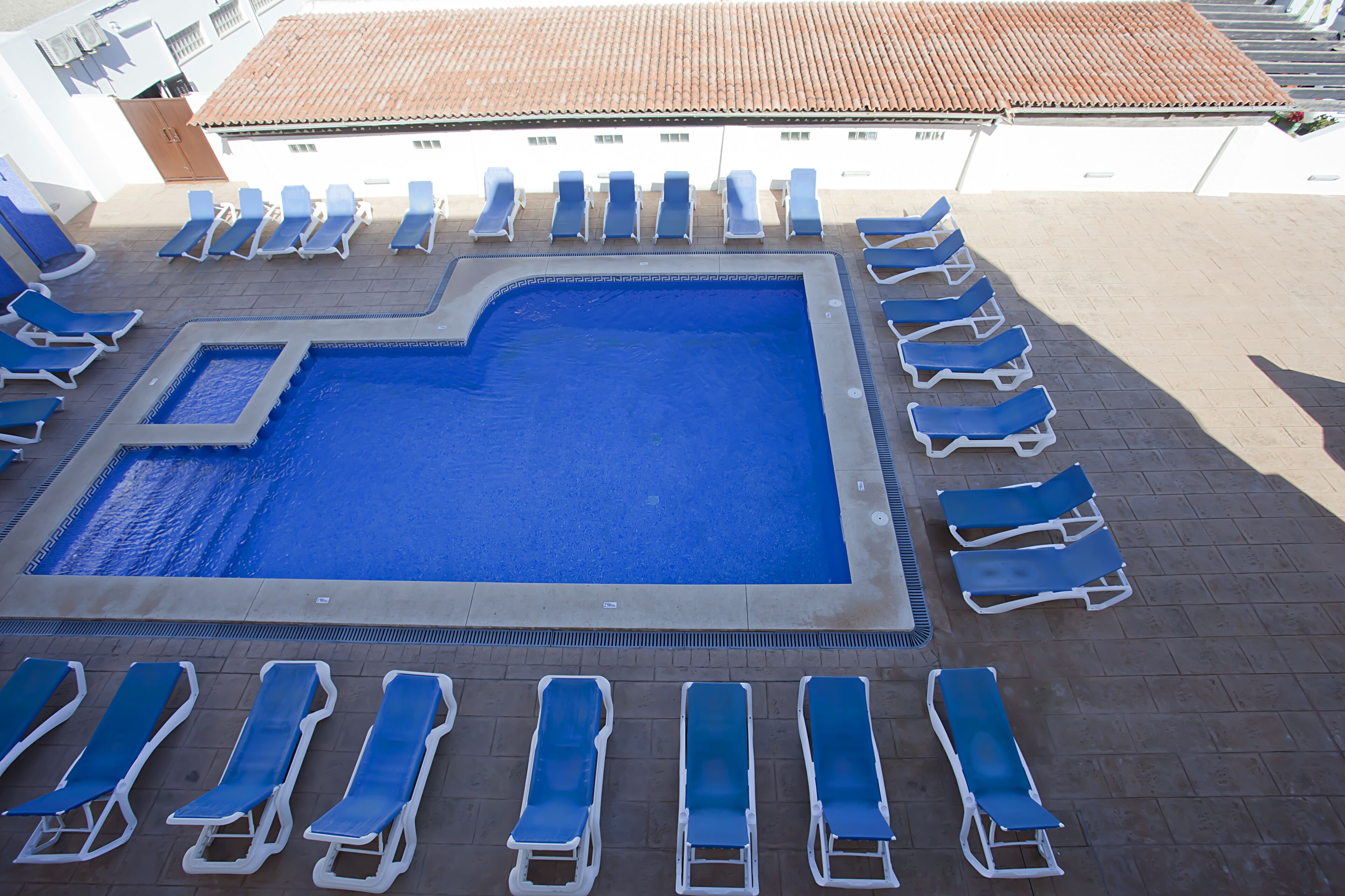 A swimming pool surrounded by sun loungers, with a tiled roof overhead.