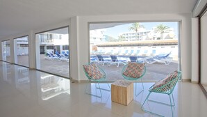 A spacious indoor area with a view of a poolside area, including lounge chairs and umbrellas. - Don Quijote (Capdepera)