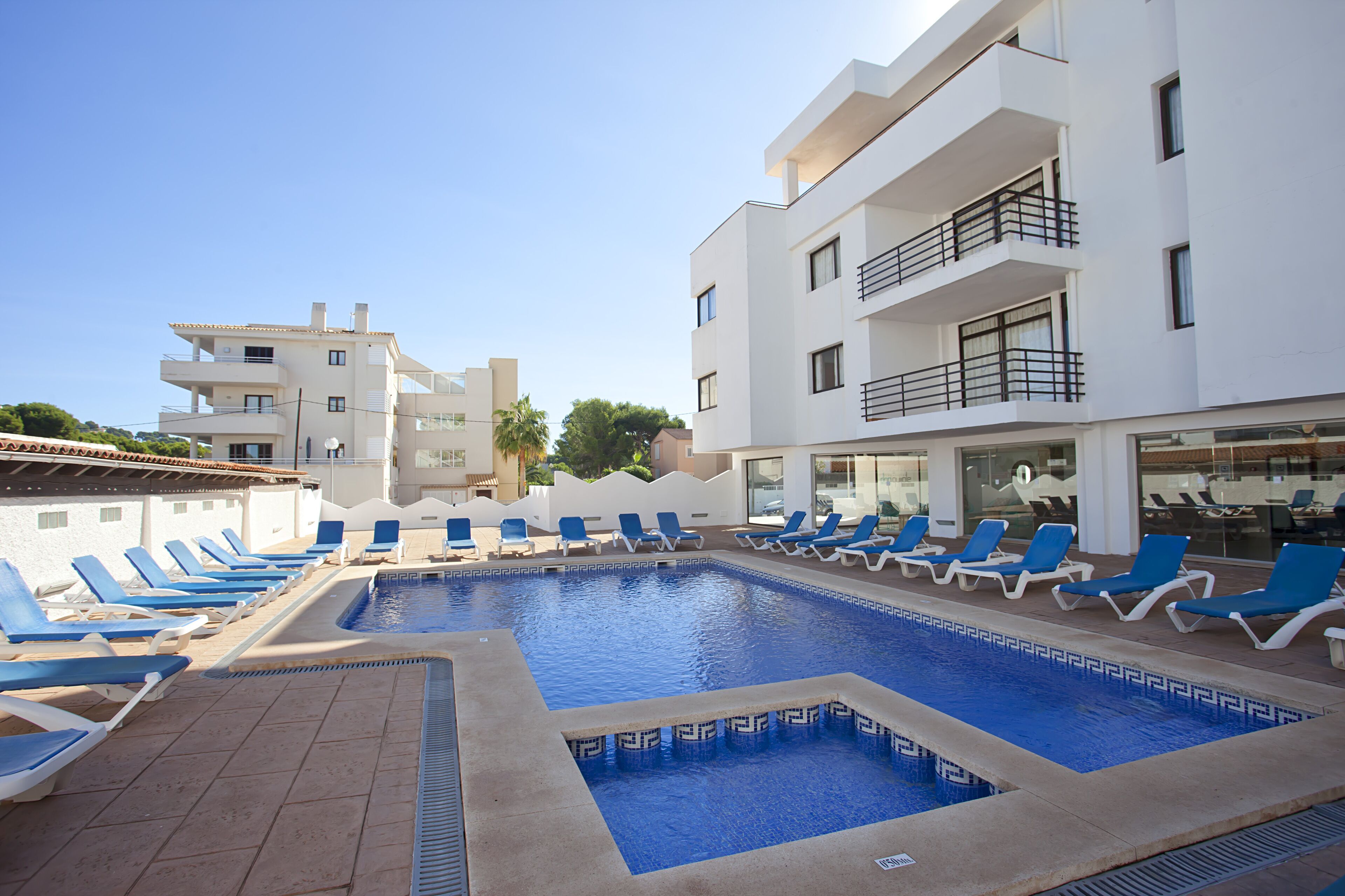 Zona de piscina con sillas reclinables azules y una piscina de color azul cristalino.