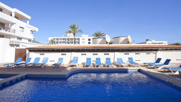 A swimming pool with blue lounge chairs and a clear blue sky. - Don Quijote (Capdepera)