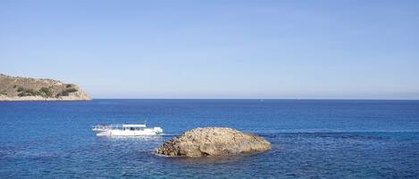 A boat on a calm sea with a rocky outcrop in the foreground and a clear sky.
