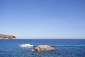 A boat on a calm sea with a rocky outcrop in the foreground and a clear sky.