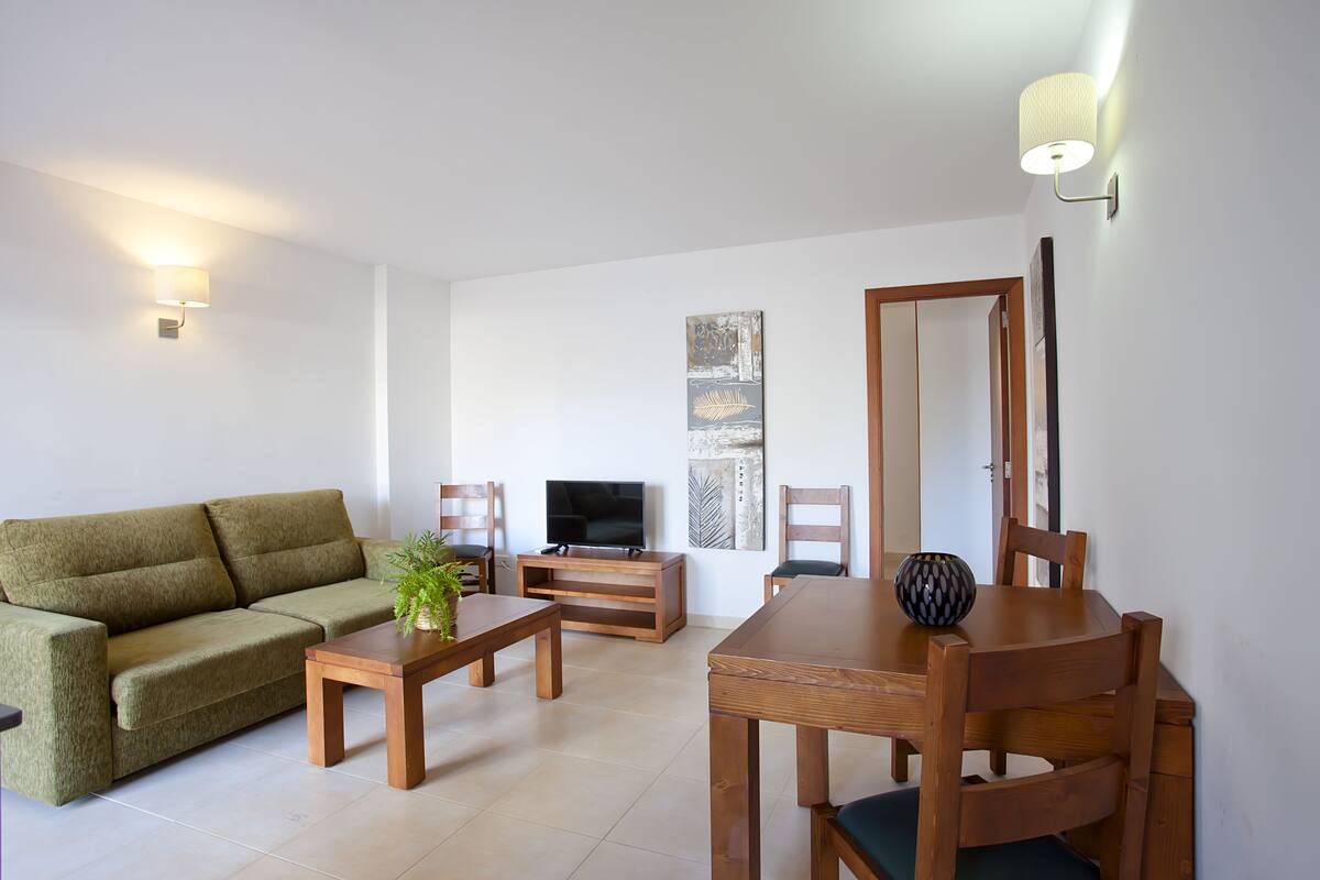 Una sala de estar con sofá, televisión, mesa de comedor de madera y sillas.