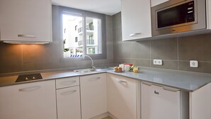 A modern kitchen with white cabinets, a stainless steel microwave, and a window with a view of a building. - Don Quijote (Capdepera)