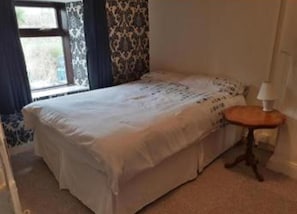 A bedroom with a bed, a small table, and a window with curtains.