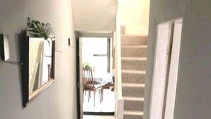 Un pasillo estrecho con una escalera a la derecha que da a un espacio exterior con sillas y una mesa.