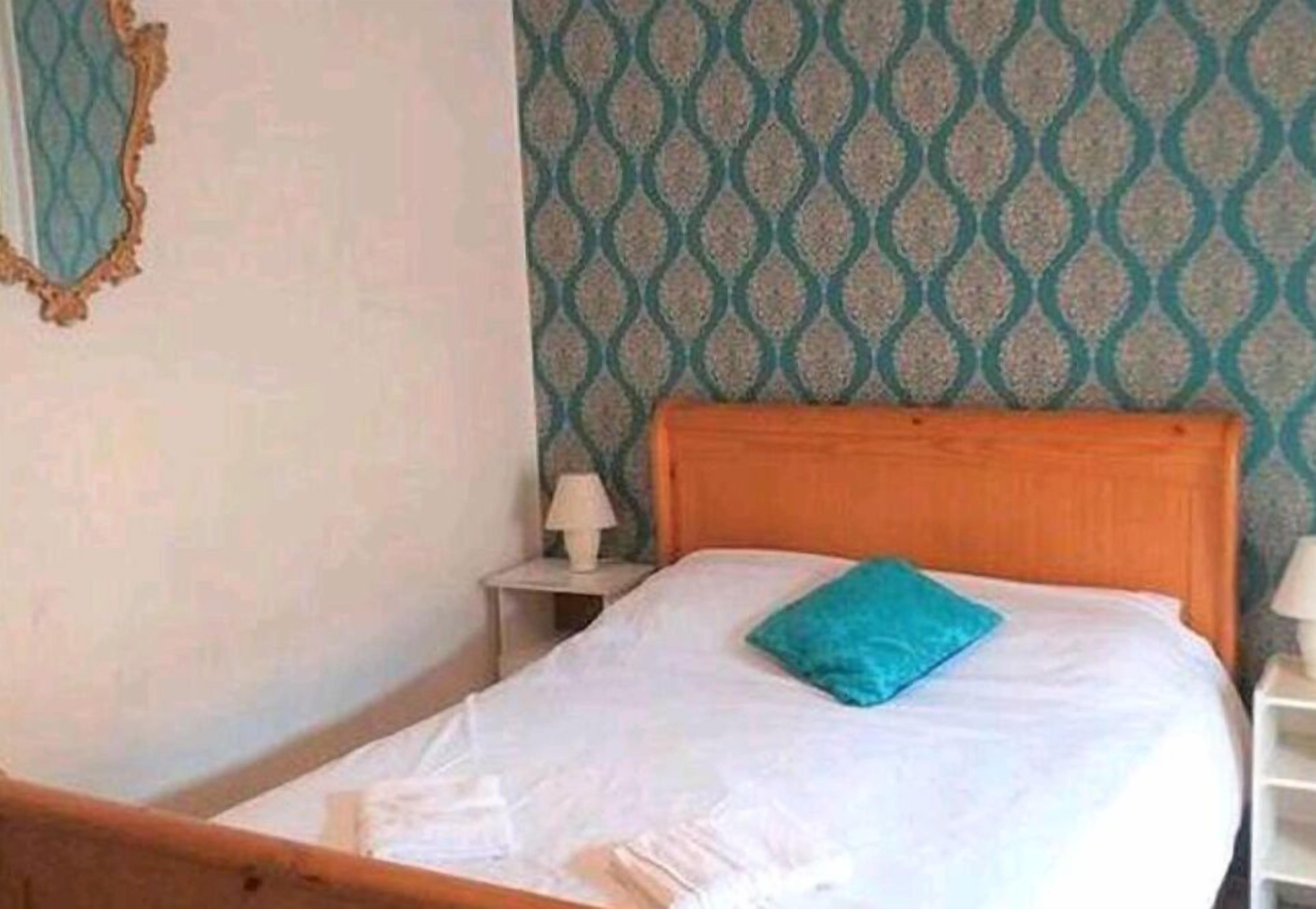 Un letto singolo con testiera in legno, un cuscino blu e una coperta bianca.
