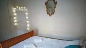 Una cama bien hecha con sábanas blancas y una almohada azul, un cabecero de madera, un espejo con marco decorativo y una guirnalda de luces en la pared.