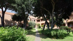 Une cour intérieure avec un chemin pavé, bordée d’une végétation luxuriante et d’arbres, qui mène à un bâtiment doté de nombreux balcons.