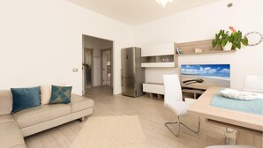 Un salon moderne comprenant un canapé, un coin repas avec une table et des chaises, un réfrigérateur et un téléviseur fixé au mur.
