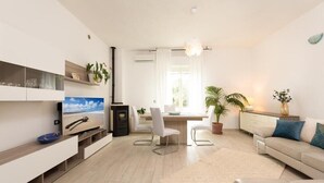 Un salon moderne doté d’un téléviseur à écran plat, d’un coin repas avec une table et des chaises en bois, d’un canapé et d’une plante en pot.