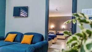 A modern hotel room with a blue sofa, two beds, and a small TV on the wall. - The Seven Apartments (St. Julian's)