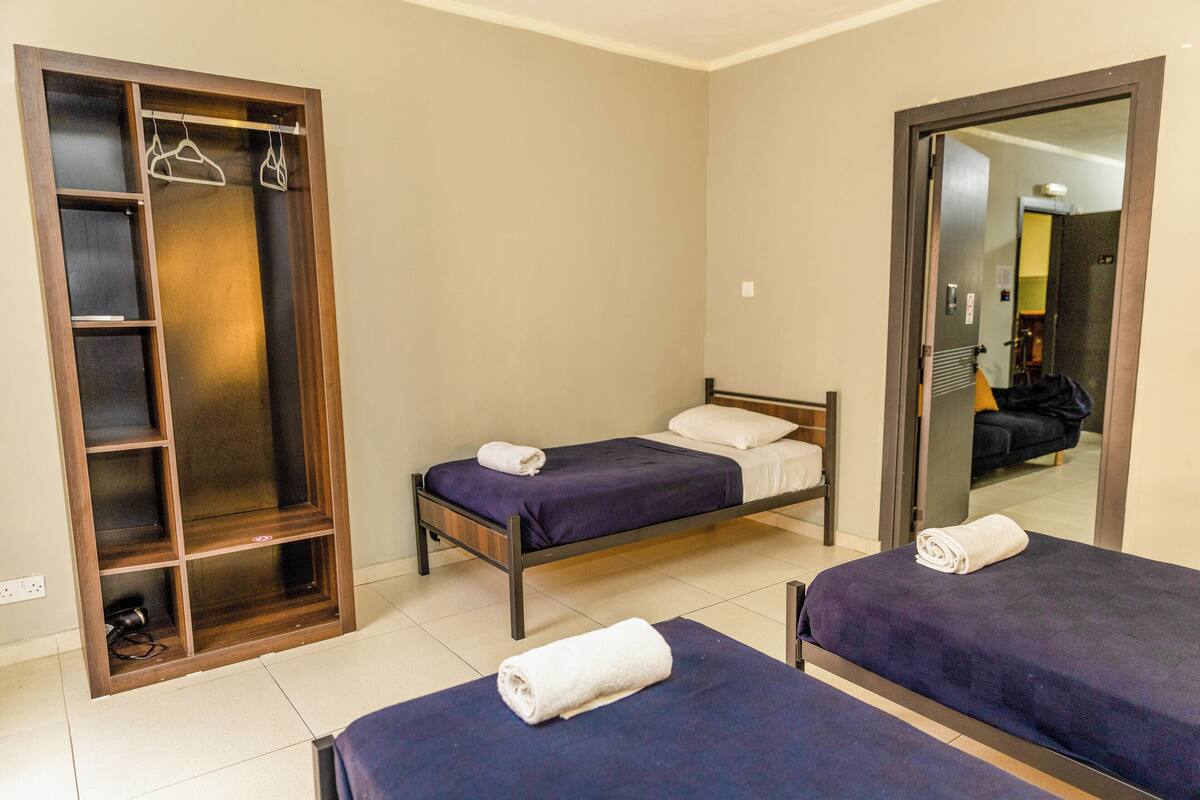 Une chambre d’hôtel avec deux lits simples, une armoire en bois avec des étagères et un miroir qui reflète la pièce.