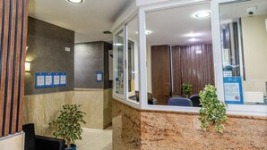 A reception area with a marble counter, a computer, and a potted plant. - The Seven Apartments (St. Julian's)