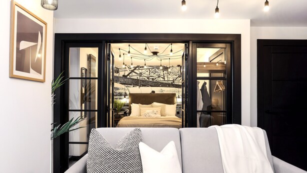 A modern living room with a sofa, pillows, and a view of a bed through an open door. - The Brewers Rooms Contemporary Aparthotel (Edinburgh)
