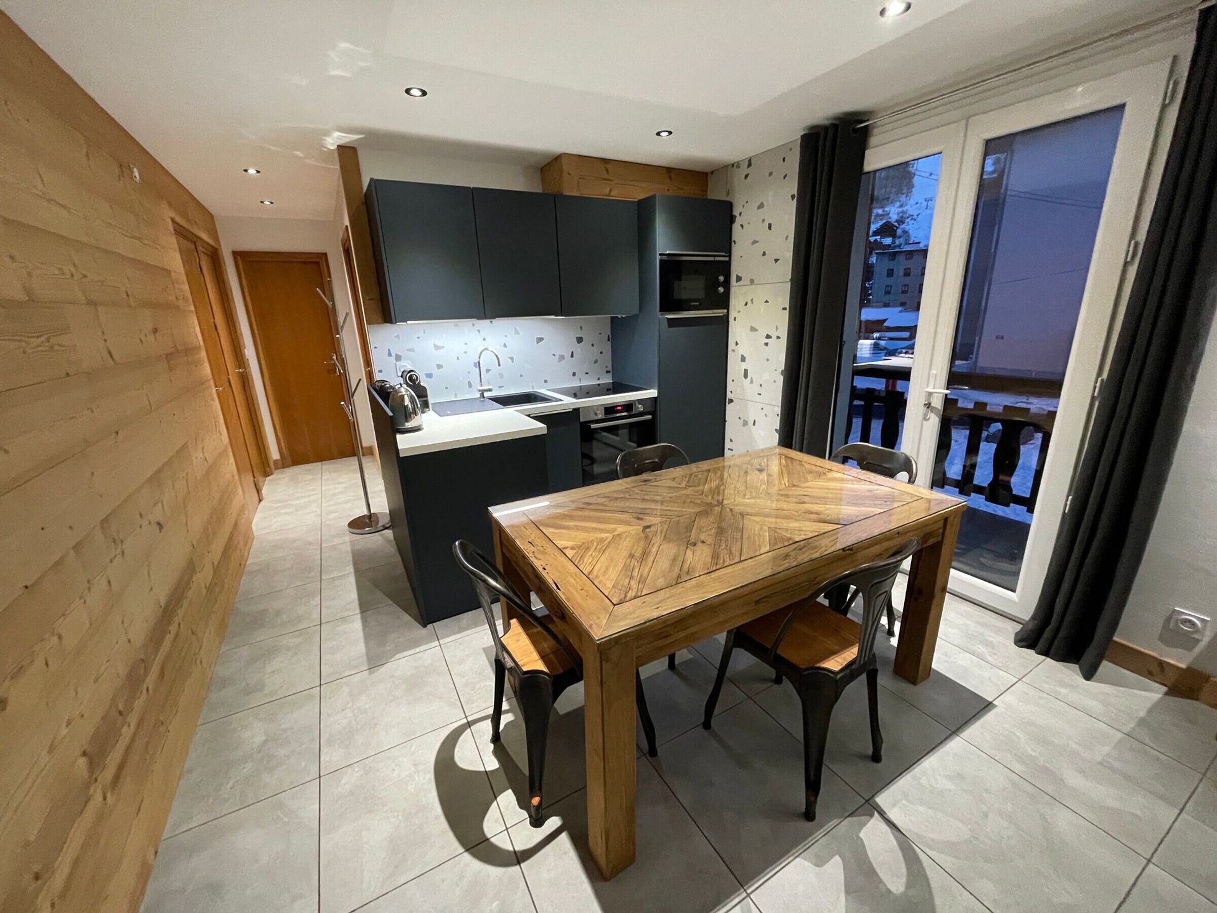 Una cocina moderna con armarios oscuros, una isla central y un comedor con mesa y sillas de madera.