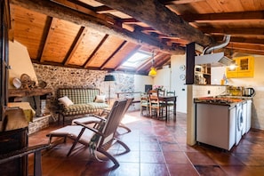 Un interior rústico con pared de piedra, vigas de madera en el techo, una zona de comedor y una cocina con lavadora.