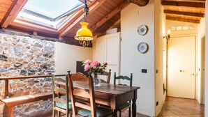 Un espace repas avec une table et des chaises en bois, un mur en pierre et une lucarne.