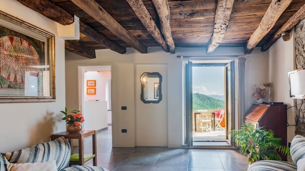 Una sala de estar con un sofá, una mesa con un florero, un espejo y una puerta que da a un balcón.
