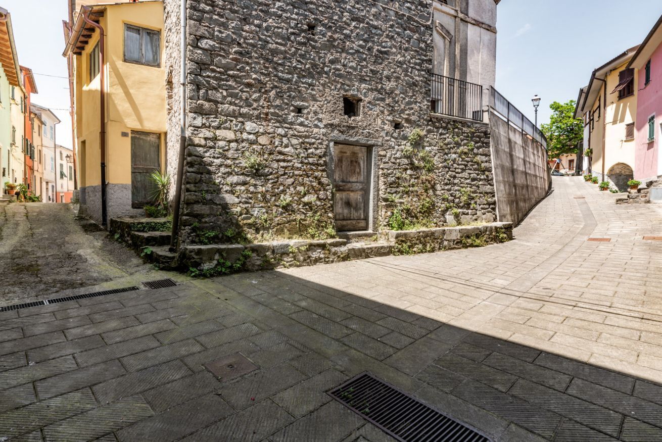 A narrow street with stone buildings, a metal gate, and a paved path.