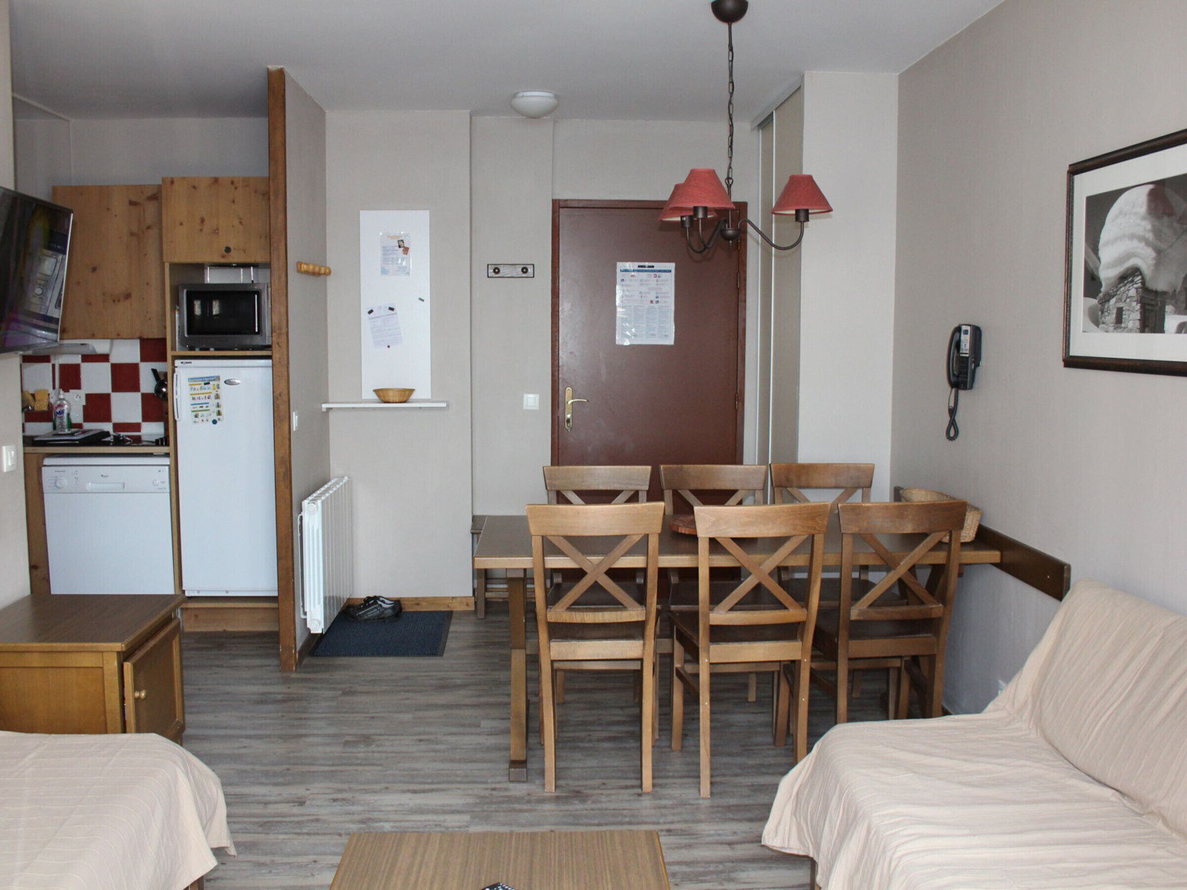 A compact living space with a kitchenette, a dining area with wooden chairs, a small table, and a bed.
