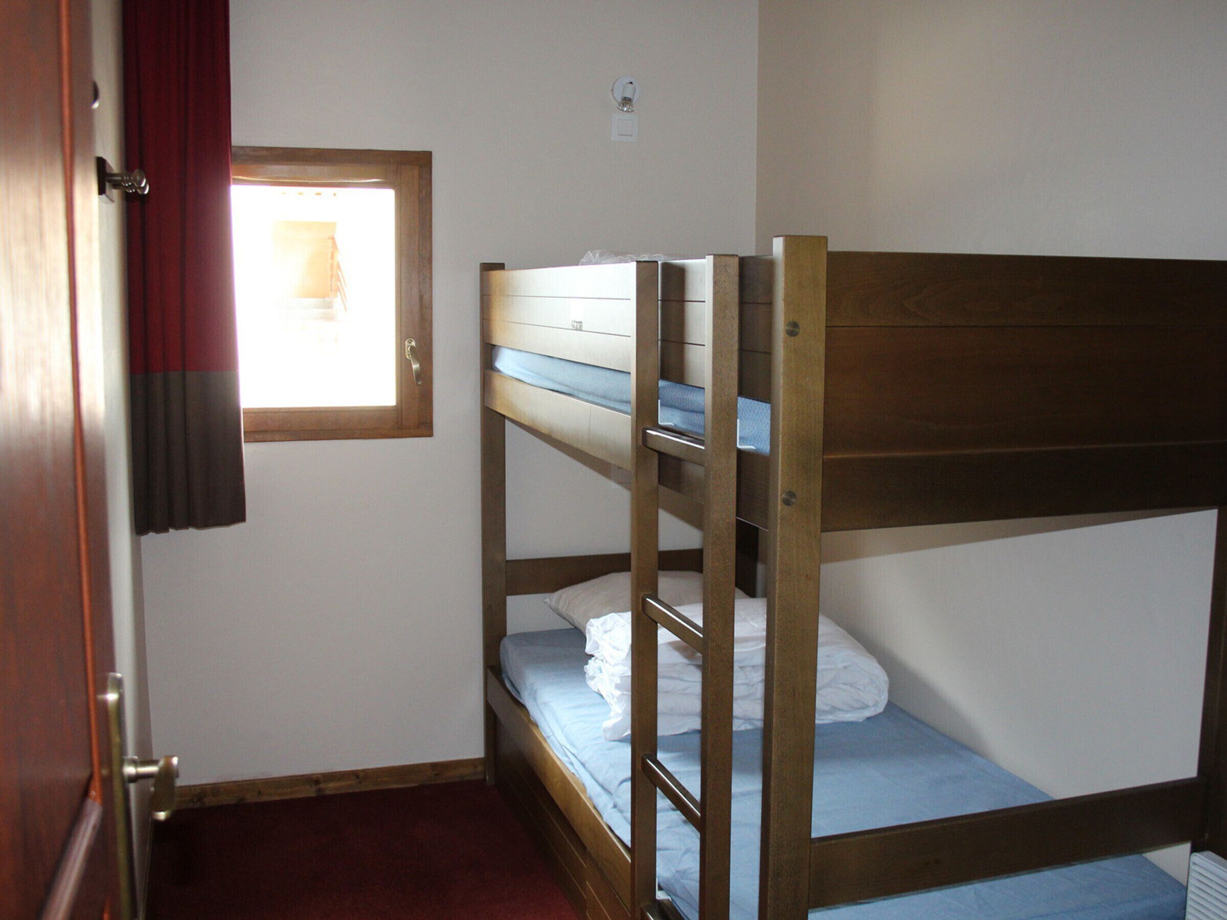 A bunk bed room with a window, a door, and a light switch on the wall.
