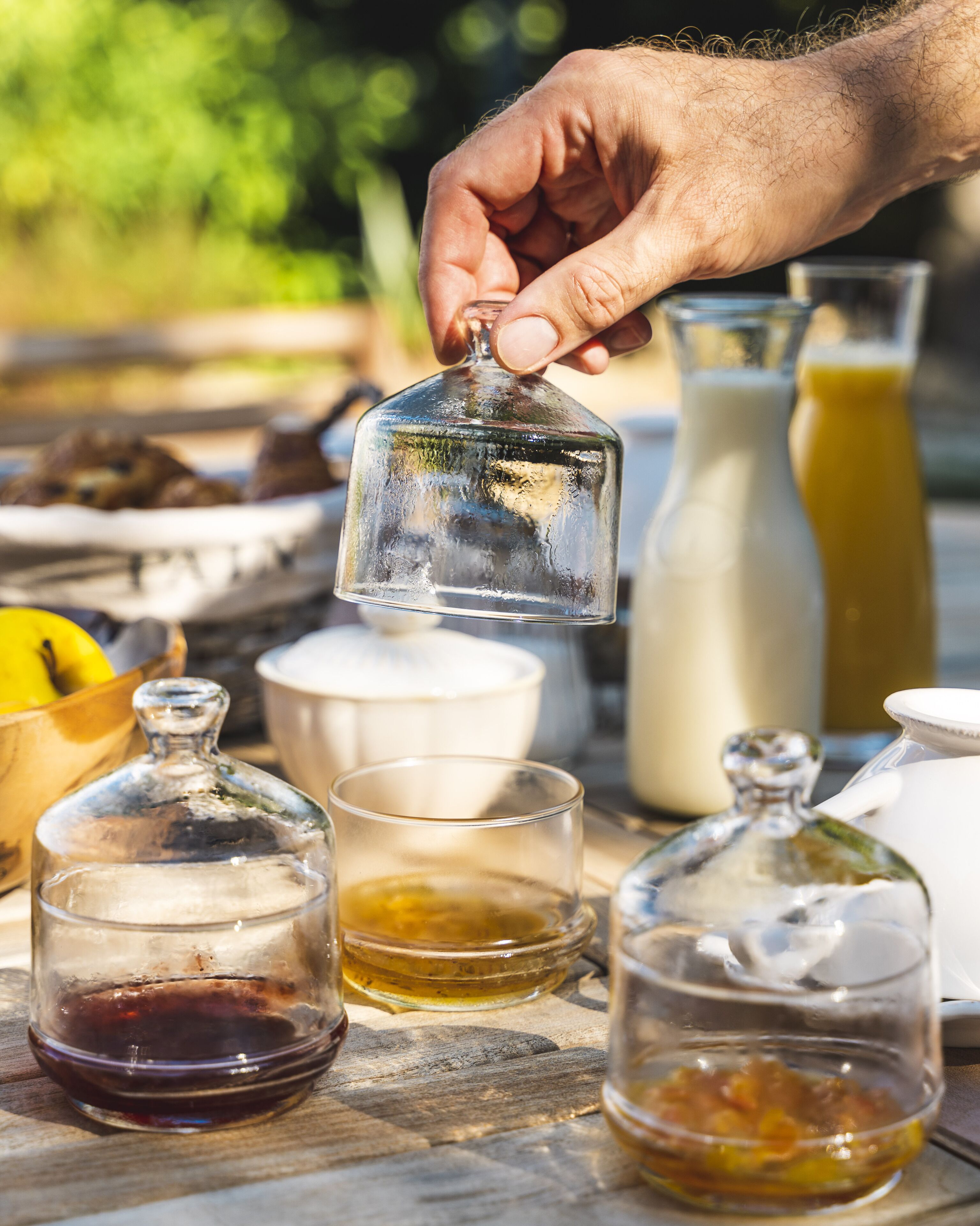 Una mano sosteniendo una campana de cristal sobre una mesa con diversos alimentos y recipientes.