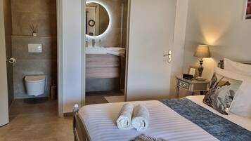 Une chambre d’hôtel comprenant un lit, une table de chevet, une lampe, une salle de bain avec un lavabo et un miroir, ainsi que des toilettes.