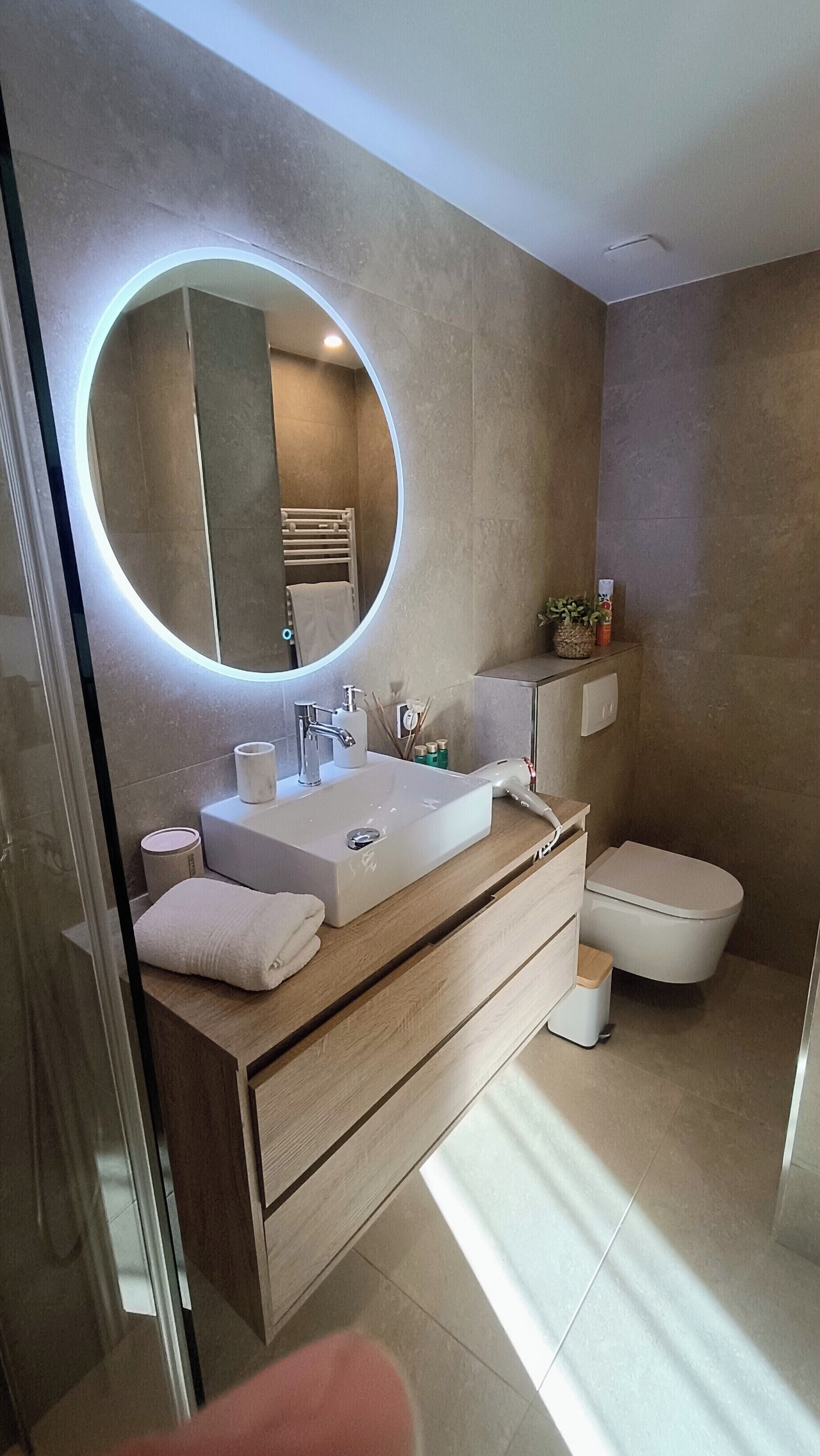 Un baño moderno con un espejo redondo, un lavabo, un inodoro y una zona de ducha.