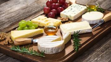 A wooden board with various cheeses, grapes, walnuts, and a small bowl of honey.